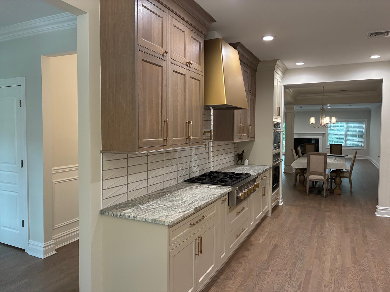 Completed custom kitchen with wood cabinetry, brass range hood, and stone counters