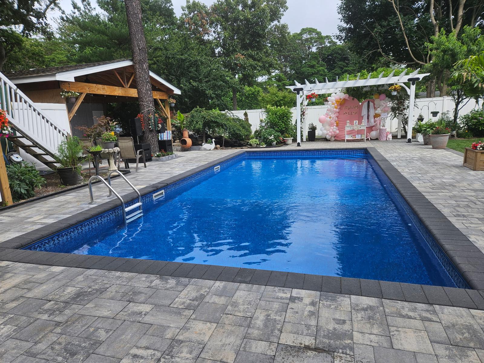 Completed pool surround with gray pavers, pergola, and covered outdoor seating